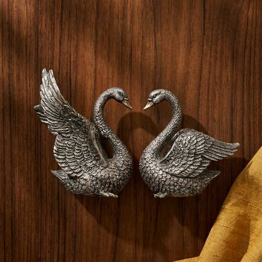 Two silver swan-shaped door handles on a wooden surface with a yellow fabric.