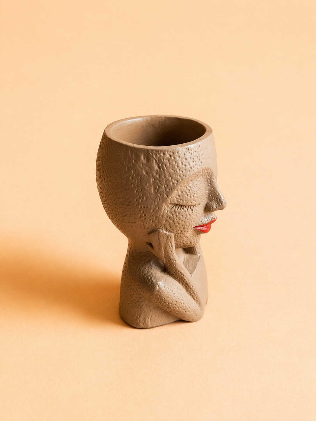 Handcrafted face planter decor featuring a feminine head with closed eyes and red lips on a beige background.